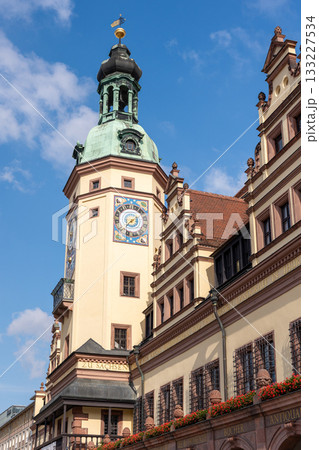 Historic tower ornate clock rises above vibrant Leipzig architecture under clear blue sky. Warm sunlight highlights detailed facade, creating vivid contrast soft clouds elegant decorative elements Historic tower ornate clock rises above vibrant Leipzig architecture under clear blue sky. Warm sunlight highlights detailed facade, creating vivid contrast soft clouds elegant decorative elements 133227534