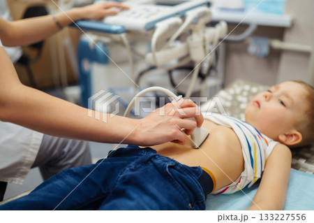Doctor conducts ultrasound examination of heart, abdominal organs of little boy using equipment. Doctor conducts ultrasound examination of heart, abdominal organs of little boy using equipment. 133227556