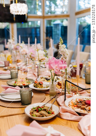 Elegant banquet table with pink peonies, taper candles and plates set for celebration 133228178