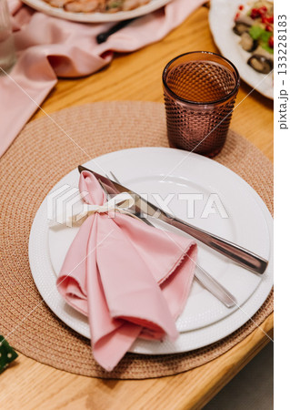 Elegant place setting with pink napkin and ribbon on woven placemat, wedding dinner decor 133228183