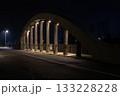 Night view of a concrete arch bridge illuminated by streetlights, with strong shadows and an empty road creating a calm urban atmosphere. 133228228
