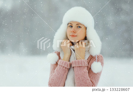 Young woman outdoors, girl in winter hat, sweater on snowy forest background with snowflakes 133228607