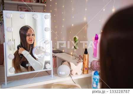 Teenager brushing long hair in illuminated vanity mirror 133228787