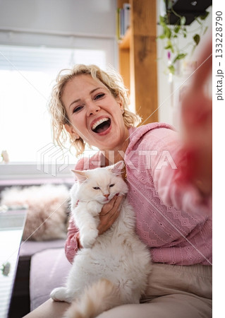 Woman laughing taking selfie with her white cat at home Woman laughing taking selfie with her white cat at home 133228790