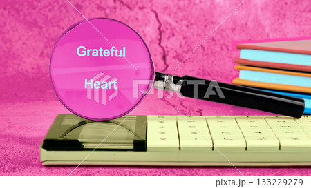 A bright scene showcases a magnifying glass highlighting the words Grateful Heart on a calculator. Colorful books stack nearby, creating a cheerful, inviting atmosphere for reflection 133229279