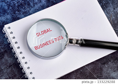 A magnifying glass focuses on the words global business 2026 in red, resting on an open notebook. This scene captures a moment of reflection on future business strategies and insights A magnifying glass focuses on the words global business 2026 in red, resting on an open notebook. This scene captures a moment of reflection on future business strategies and insights 133229288