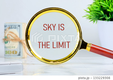 A golden magnifying glass displays the phrase sky is the limit, symbolizing endless possibilities. Nearby, a bundle of cash and a potted plant enhance the theme of growth and success 133229308