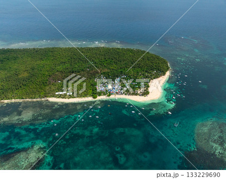 Coastal village with clustered houses surrounded by tropical forest and boats anchored near the beach. Daku Island. Siargao, Philippines. 133229690