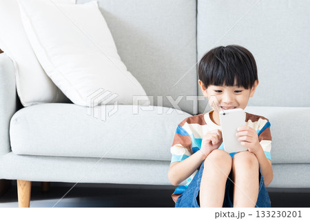 リビングでスマホで遊ぶ小学生男子 リビングでスマホで遊ぶ小学生男子 133230201