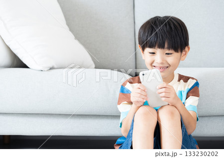 リビングでスマホで遊ぶ小学生男子 リビングでスマホで遊ぶ小学生男子 133230202