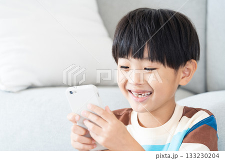 リビングでスマホで遊ぶ小学生男子 リビングでスマホで遊ぶ小学生男子 133230204