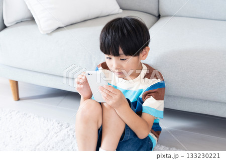 リビングでスマホで遊ぶ小学生男子 リビングでスマホで遊ぶ小学生男子 133230221