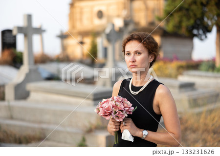 Woman in black dress with bouquet of flowers came to cemetery to honor the memory of deceased loved one Woman in black dress with bouquet of flowers came to cemetery to honor the memory of deceased loved one 133231626