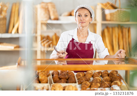 Selling fresh croissants in bakery - female baker places hot croissants on display Selling fresh croissants in bakery - female baker places hot croissants on display 133231876