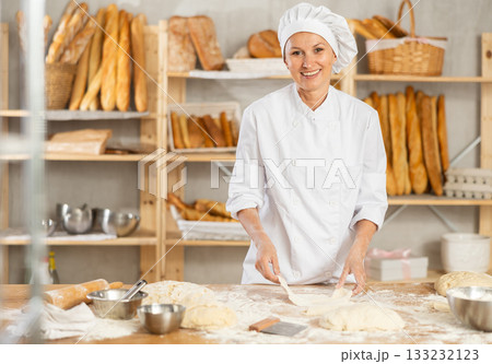 Professional female baker preparing pizza dough in bakery 133232123