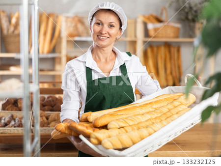 Female baker worker sells baguette, shows many products 133232125