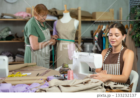 Female seamstress working on a typewriter against the background of a dressmaker and a mannequin 133232137