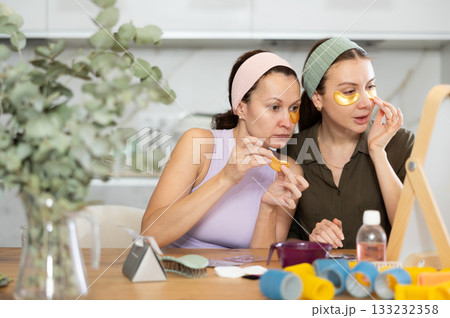 Two female friends applying golden under-eye patches at home 133232358
