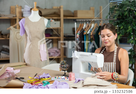 Female seamstress working on a machine against the background of a mannequin 133232586