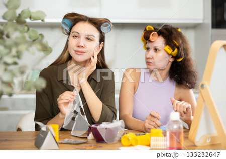 Two women testing out hydrating face paper mask at home Two women testing out hydrating face paper mask at home 133232647