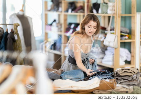 Positive young girl choosing jeans pantaloons in clothing store 133232658