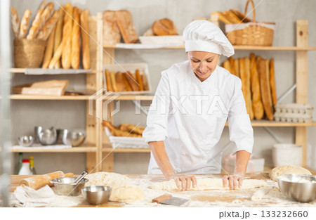 Process of making baguette, loaf or bread in bakery - female baker kneads and rolls dough to give shape of future bread 133232660