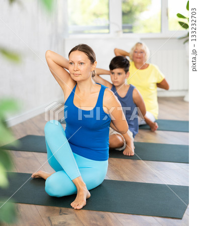 Middle-aged woman practicing cow face pose of yoga in light fitness room 133232703