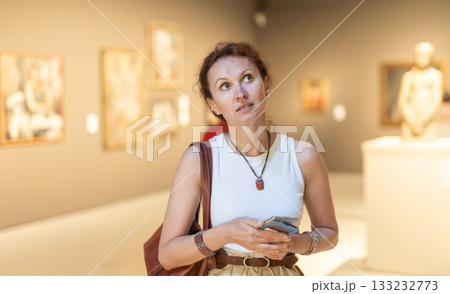 Woman with phone looking at art gallery Woman with phone looking at art gallery 133232773