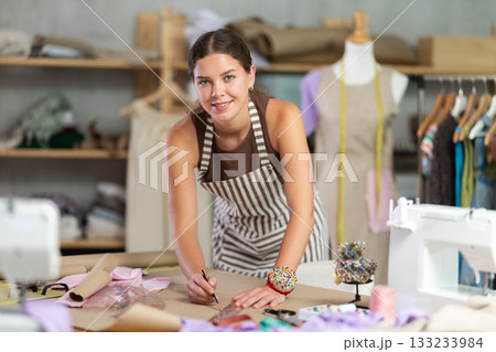 Female fashion designer drawing on paper with curved rulers in workshop 133233984