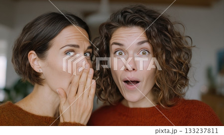 Two women sharing a secret with natural expressions in a cozy indoor setting 133237811