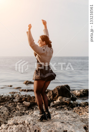 Woman Dancing Ocean Rocks Sunset: Joyful coastal celebration, sunlit seaside dance. 133238561