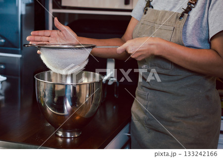 Woman sifting the flour into a metal bowl for making dough. Woman sifting the flour into a metal bowl for making dough. 133242166