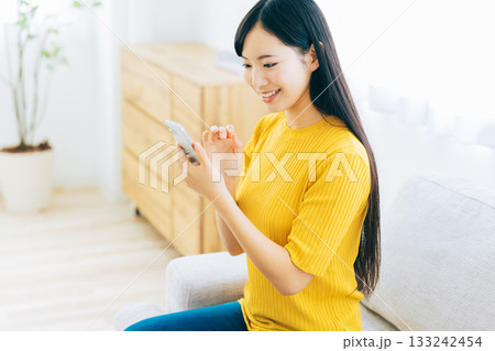 ソファでスマホを見る若い女性 133242454