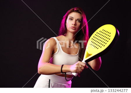 Woman practicing tennis with a large paddle in a dark studio setting 133244277