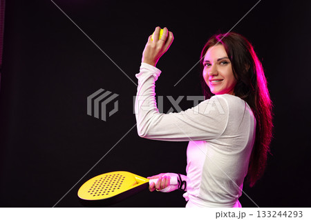 Young woman practicing with a paddle and ball in a dark studio setting with vibrant lighting Young woman practicing with a paddle and ball in a dark studio setting with vibrant lighting 133244293