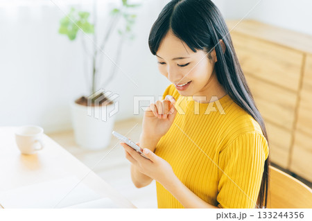 リビングでスマホを見る若い女性 133244356