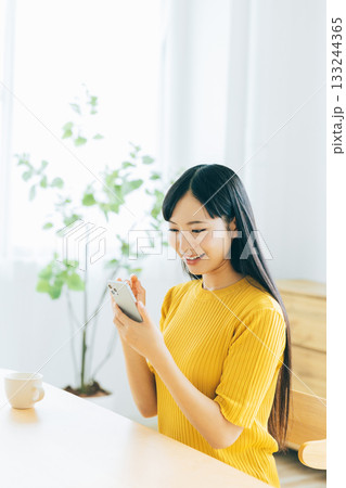 リビングでスマホを見る若い女性 133244365