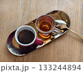 A cup of coffee and a cup of tea served on a golden tray with a spoon on a wooden table.  133244894