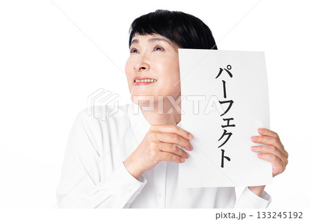 パーフェクトと書かれた紙を両手で持ち嬉しそうに微笑む白いシャツを着たシニア女性 133245192