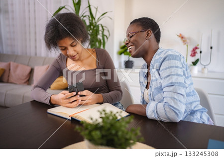 Two young black women laughing while looking at smartphone at home 133245308
