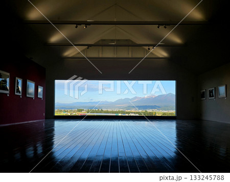 The gallery's polished wooden floor reflects the stunning view of mountains and a vibrant sky, creating a unique perspective The gallery's polished wooden floor reflects the stunning view of mountains and a vibrant sky, creating a unique perspective 133245788