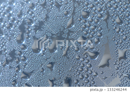 Raindrops dance on a window glass, creating a mesmerizing pattern under soft indoor lighting 133246244