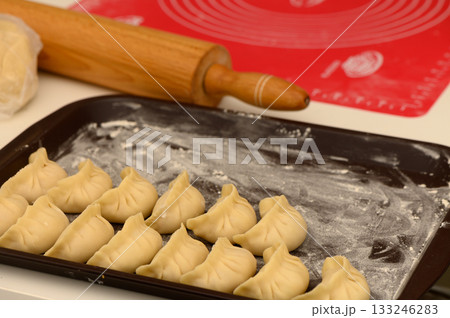 Homemade dumplings arranged neatly on a baking tray with a rolling pin in a cozy kitchen setting 133246283