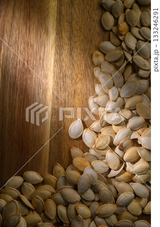 Brightly lit pumpkin seeds scattered on a wooden surface drying in the warm afternoon sun Brightly lit pumpkin seeds scattered on a wooden surface drying in the warm afternoon sun 133246291