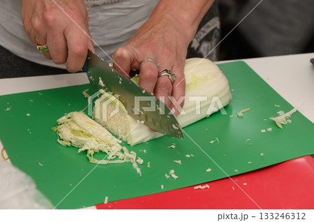 Cutting fresh cabbage on a green cutting board in a bright kitchen during a cooking class 133246312