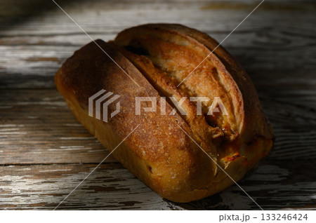 Warmly baked loaf resting on rustic wooden surface in soft afternoon light 133246424