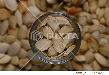 Pumpkin seeds in a glass jar surrounded by a pile of seeds in cozy autumn setting 133246437