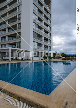 Sunny day at a sleek modern hotel with a sparkling pool and cloudy skies above Sunny day at a sleek modern hotel with a sparkling pool and cloudy skies above 133246509