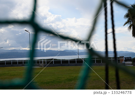 Scenic view through a goal net at a peaceful lakeside park during a cloudy afternoon 133246778