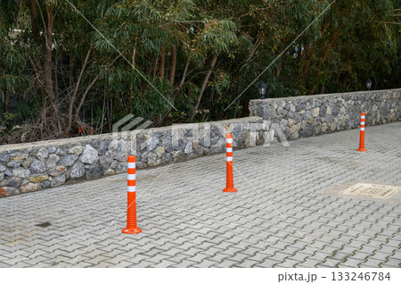 Bright orange cones mark off a parking area beside a stone wall and lined trees during a calm afternoon 133246784